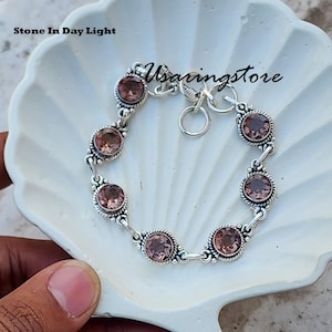 May include: A silver bracelet with a clasp closure features a row of six round, pink gemstones. The bracelet is displayed on a white seashell-shaped surface. The text "Stone In Day Light" and "Usaringstore" are visible in the image.