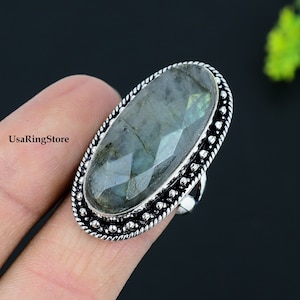 Puede incluir: Un anillo de plata con una gran piedra ovalada de labradorita. El anillo tiene un borde con cuentas y una banda texturizada.