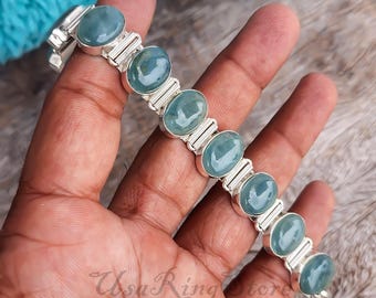 May include: A silver bracelet featuring oval, light blue gemstones. The gemstones are set in a silver band with rectangular accents. The bracelet is displayed on a hand.