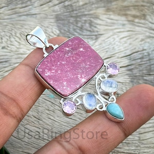 Peut inclure: Un pendentif en argent avec une pierre précieuse rose et blanche, un design argenté délicat et de petites pierres précieuses roses, bleues et blanches.