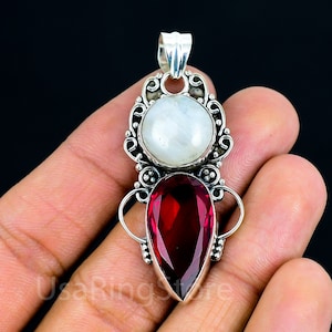 May include: A silver pendant with a white moonstone and a red gemstone. The pendant is set in a silver filigree design.