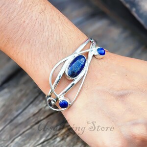 May include: A silver cuff bracelet with a blue lapis lazuli stone set in the center and two smaller blue stones on the sides.