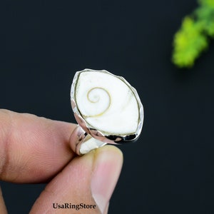 May include: A silver ring with a white shell inlay. The shell has a spiral pattern.