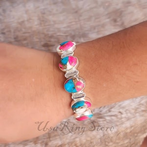 May include: A silver bracelet with oval-shaped stones in shades of pink, turquoise, and white. The bracelet is composed of multiple stones connected by silver links. The text "Usa Ring Store" is visible at the bottom of the image.