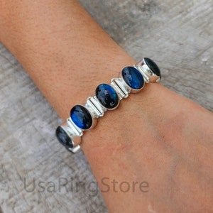Puede incluir: Un brazalete de plata con piedras azules ovaladas. El brazalete tiene un diseño de eslabones.