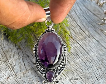 May include: A silver pendant featuring a large oval-shaped purple amethyst gemstone and a smaller teardrop-shaped amethyst stone at the base. The metal setting is decorated with small silver beads and wire detailing. The text UsaRingStore is visible.
