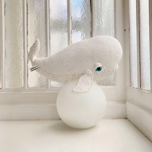 May include: A white plush whale toy with blue eyes sits on top of a white round lamp. The whale has a speckled texture and the text "Pippa & Co." is visible on the side.