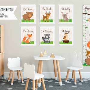May include: A set of six framed woodland animal prints with inspirational phrases like "Be Brave" and "Be Kind".  A growth chart with a woodland animal theme is also included. The growth chart is labeled "Anniston 5" and features a variety of woodland animals, including a deer, a fox, a raccoon, an owl, and a bear. The growth chart is printed on a woodgrain background.