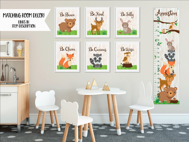 May include: A set of six framed woodland animal prints with inspirational phrases like "Be Brave" and "Be Kind".  A growth chart with a woodland animal theme is also included. The growth chart is labeled "Anniston 5" and features a variety of woodland animals, including a deer, a fox, a raccoon, an owl, and a bear. The growth chart is printed on a woodgrain background.