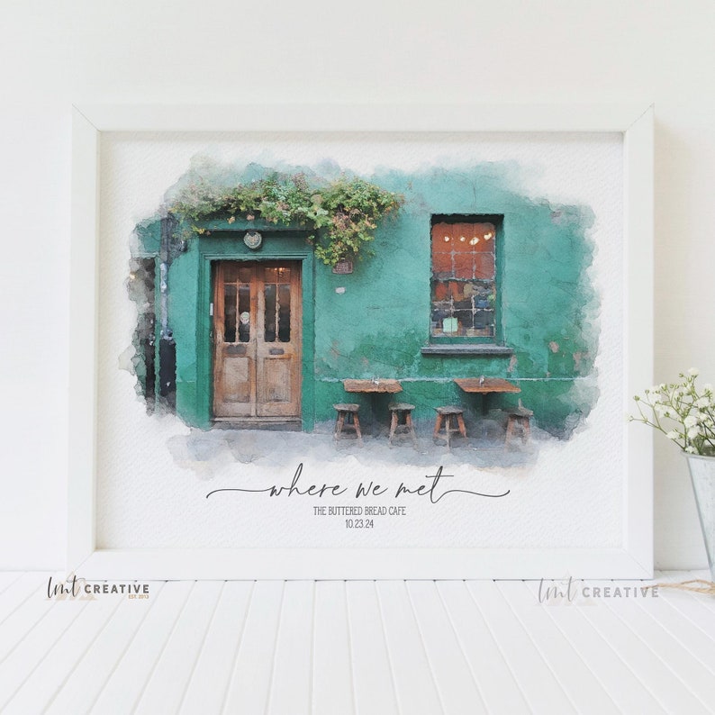 May include: A watercolor painting of a green building with a wooden door and a window. The building has a sign that says "The Buttered Bread Cafe" and the date "10.23.24". The text "where we met" is written in cursive below the sign.