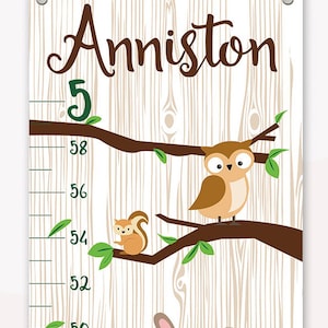 May include: A white wooden growth chart with a brown branch and green leaves. The chart features a brown owl, a brown squirrel, and a brown rabbit. The chart is labeled with the name "Anniston" and has measurements in inches from 50 to 58.