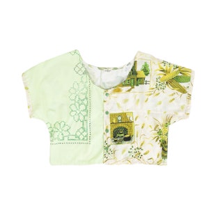 May include: A patchwork top with short sleeves. One side is light green with green floral embroidery. The other side features a vintage print with a cottage, corn, and wheat in shades of green and yellow. The top has green buttons.