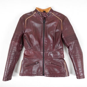 May include: A burgundy leather motorcycle jacket with a yellow trim. The jacket has a zip closure and multiple pockets.