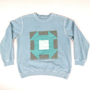 Peut inclure: Un sweat-shirt bleu clair avec un motif de patchwork vert et marron sur le devant.
