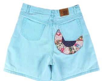 Könnte beinhalten: Hellblaue Jeans-Shorts mit einem Patchwork-Stoffdesign auf der Gesäßtasche. Die Shorts haben ein braunes Etikett mit der Aufschrift "South West Blue".