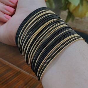 May include: A stack of black and gold bangles. The bangles are thin and have a shiny finish.