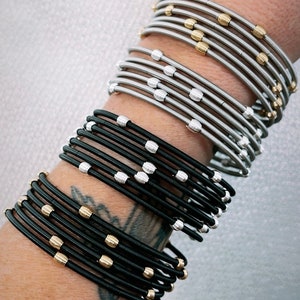 May include: A stack of silver and black bangle bracelets with gold accents. The bracelets are made of thin metal and have a stretchy design.