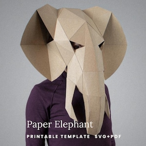 May include: A geometric elephant mask constructed from tan paper, featuring large ears and a trunk. The text smagapaperwood, Paper Elephant, and PRINTABLE TEMPLATE SVG+PDF are visible on the image. The mask is worn over a dark purple shirt.