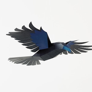 Puede incluir: Un p&aacute;jaro de papel negro y azul con las alas extendidas en vuelo. El p&aacute;jaro est&aacute; hecho de papel doblado y tiene un aspecto realista.