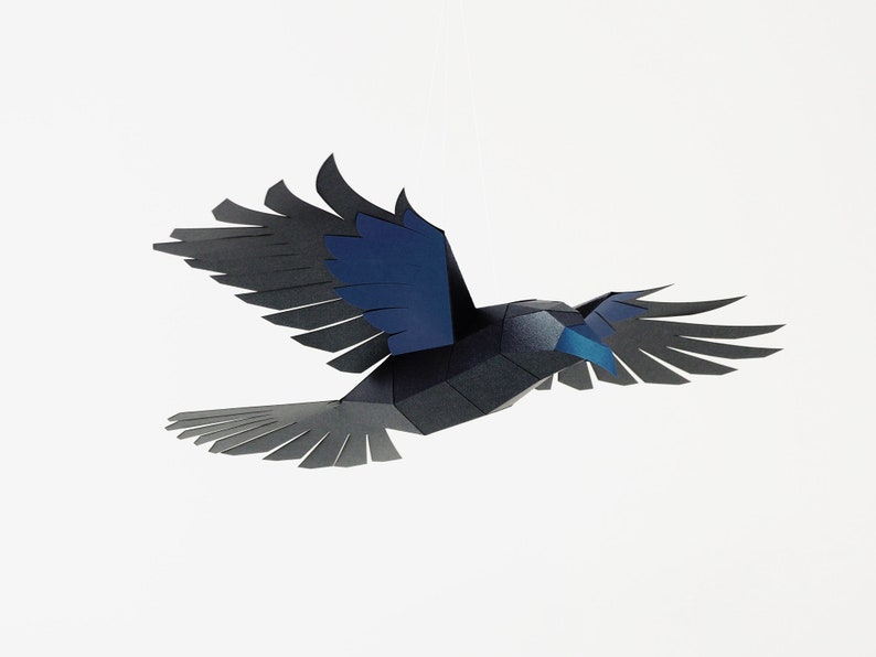 Puede incluir: Un p&aacute;jaro de papel negro y azul con las alas extendidas en vuelo. El p&aacute;jaro est&aacute; hecho de papel doblado y tiene un aspecto realista.