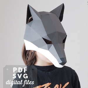 May include: A child wearing a gray and white paper wolf mask. The mask is made of paper and has a 3D design. The mask is available as a digital download in PDF and SVG formats.