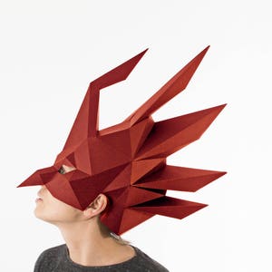 K&ouml;nnte beinhalten: Eine geometrische, rote Drachenmaske mit scharfen Winkeln und spitzen Merkmalen. Die Maske bedeckt Kopf und Gesicht, mit sichtbaren Augen&ouml;ffnungen. Das Design ist eckig und modern, geeignet f&uuml;r Cosplay oder Kost&uuml;mveranstaltungen.