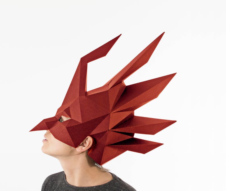 K&ouml;nnte beinhalten: Eine geometrische, rote Drachenmaske mit scharfen Winkeln und spitzen Merkmalen. Die Maske bedeckt Kopf und Gesicht, mit sichtbaren Augen&ouml;ffnungen. Das Design ist eckig und modern, geeignet f&uuml;r Cosplay oder Kost&uuml;mveranstaltungen.