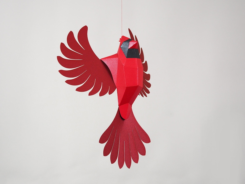 Peut inclure: Un cardinal en papier rouge avec des yeux noirs, suspendu &agrave; une ficelle. Le cardinal est fait de papier pli&eacute; et a un effet 3D.