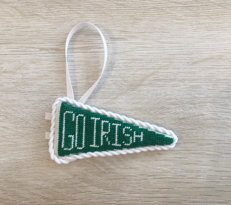 May include: Green felt pennant with white rope trim and the words "GO IRISH" embroidered in white. The pennant has a white ribbon loop for hanging.