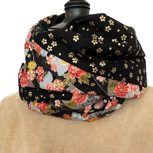 Peut inclure: Écharpe infinie noire avec un motif floral. L'écharpe présente un motif de fleurs dorées sur fond noir et une section avec des fleurs rouges, roses et jaunes. L'écharpe est enroulée autour d'un mannequin.