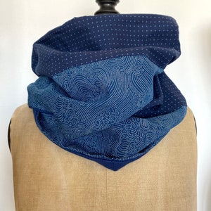 Peut inclure: Un snood bleu marine avec un design superposé. La couche supérieure présente un motif à petits points blancs, tandis que la couche intermédiaire affiche un motif en forme de vagues blanches. Le snood est présenté sur un mannequin.