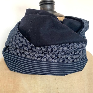 Peut inclure: Écharpe infinie bleu marine avec une bordure à motifs géométriques. La bordure présente un motif d'éclat d'étoile répété en points blancs au-dessus d'une bordure rayée. L'écharpe est présentée sur un mannequin.