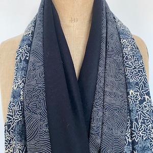 Op de afbeelding: Een zwarte sjaal met blauwe en witte patronen. De sjaal heeft een effen zwart middenpaneel, geflankeerd door panelen met een wit gestippeld golfpatroon en een blauw bloemmotief. De sjaal is over een mannequin gedrapeerd.