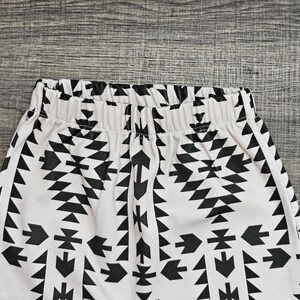 May include: White and black patterned leggings. The leggings have a repeating geometric design in black against a white background. The waistband is elasticated. The fabric appears to be soft and comfortable.