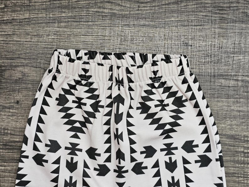 May include: White and black patterned leggings. The leggings have a repeating geometric design in black against a white background. The waistband is elasticated. The fabric appears to be soft and comfortable.