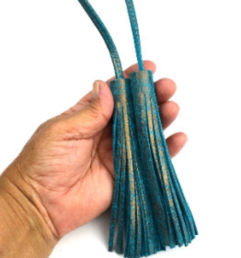 May include: Two turquoise-colored tassels with bronze accents. The tassels are made of a soft, suede-like material and are attached to a thin cord. The tassels are approximately 5 or 6 inches long.