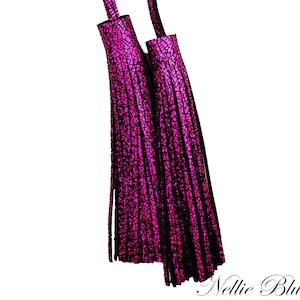 May include: Two hanging tassels featuring a vibrant magenta and black crackled texture. Each tassel consists of numerous thin, vertical strips attached to a cylindrical top piece. The text Nellie Blue's Place is visible in the bottom right corner.
