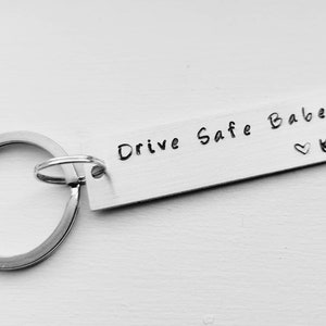 May include: Silver keychain with a rectangular tag that reads "Drive Safe Babe" with a heart and the letter "K" engraved on it.