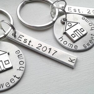Peut inclure: Porte-clés en argent avec des breloques en forme de maison et des barres gravées "Est. 2017" et "Sweet Home".