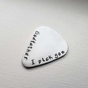 May include: Silver guitar pick with the text "Godfather I pick you" engraved on it.