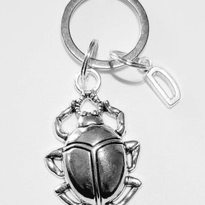 May include: Silver keyring with a silver scarab beetle charm and a silver charm with the letter D.