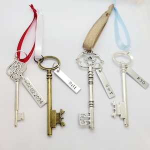May include: Four antique-style skeleton keys with decorative tags. The tags are personalised with the text "Bill", "02.02.2024", "#30", and "S&T". The keys are attached to different coloured ribbons.