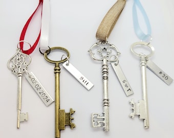 Puede incluir: Cuatro llaves esqueleto de estilo antiguo con etiquetas decorativas. Las etiquetas están personalizadas con el texto "Bill", "02.02.2024", "#30" y "S&T". Las llaves están unidas a cintas de diferentes colores.