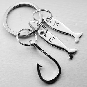 May include: Silver keychain with a fish hook charm and two fish charms with the letters "M" and "E" engraved on them.