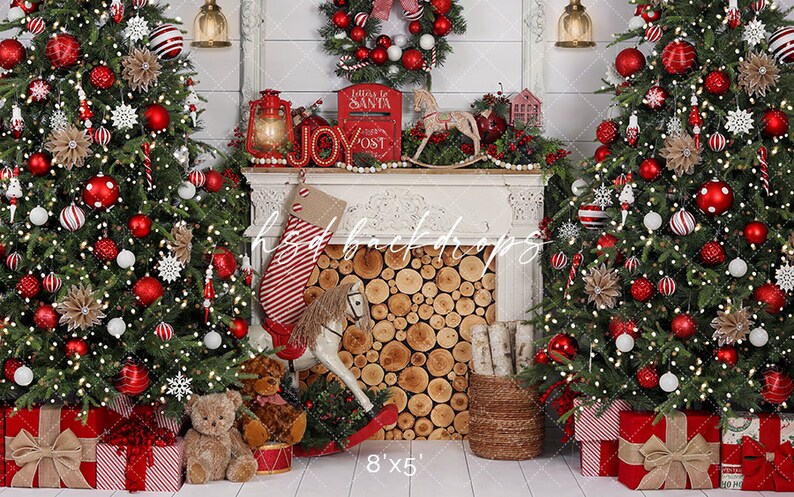 May include: A festive Christmas backdrop featuring two decorated trees with red and white baubles, garlands, and lights. A fireplace mantel displays a wreath, lantern, and a "JOY" sign. Presents and a rocking horse are at the base.