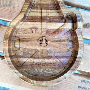 Pode incluir: Uma tigela de servir de madeira em forma da nave espacial Millennium Falcon de Star Wars. A tigela é feita de madeira clara e escura e tem uma escultura detalhada do exterior da nave espacial.