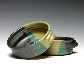 May include: Two ceramic bowls with a black, green, and yellow glaze. The bowls are stacked on top of each other.