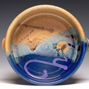 May include: A ceramic bowl with a blue, brown, and white glaze. The bowl has two handles and a purple swirl design on the inside.