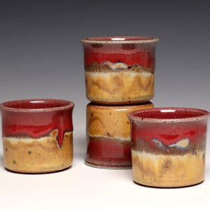 May include: Four ceramic mugs with a red and yellow glaze. The mugs are stacked in a pyramid shape.