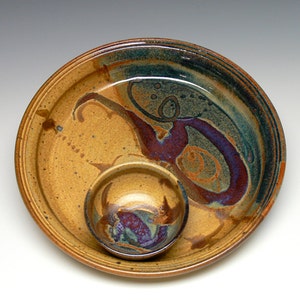 May include: A handmade ceramic serving set featuring a large plate and a small bowl. The set has a speckled tan base with abstract designs in teal, purple, and orange. The plate measures approximately 12 inches in diameter.